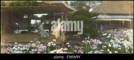 Ein Foto mit zwei jungen Frauen in einem traditionellen japanischen Pavillon in einem Garten. Das Bild ist handkoloriert und zeigt die lebendige Schönheit des Gartens und der Damenbekleidung. Stockfoto