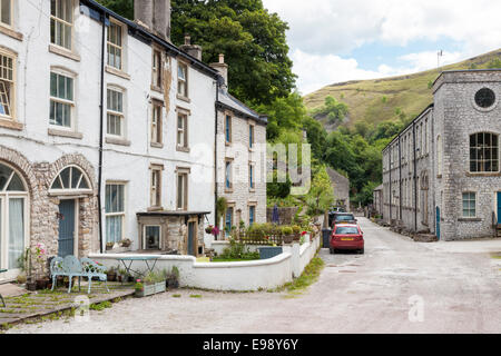 Die Straße und eine Reihe von terrassenförmig angelegten Cottages mit der Mühle (rechts) in der Ortschaft Litton Mill, Derbyshire, England, Großbritannien Stockfoto