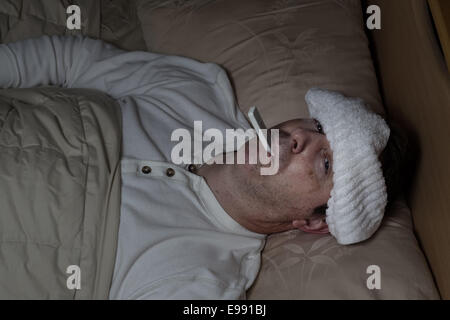 Horizontales Bild des reifen Mannes, mit nassen Handtuch auf Stirn, liegend im Bett testen seine Temperatur Stockfoto