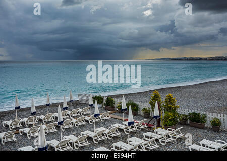 Weißen Liegestühlen am menschenleeren Strand bei schlechtem Wetter mit dunklen, bedrohlichen Regenwolken über dem Meer Stockfoto