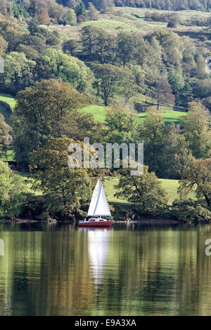 Eine kleine Yacht in vollen Segeln (mit Reflexion) auf See Coniston im Lake District, Cumbria, Großbritannien Stockfoto