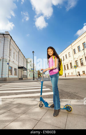 Kleine lächelndes Mädchen steht auf Roller in der Stadt Stockfoto