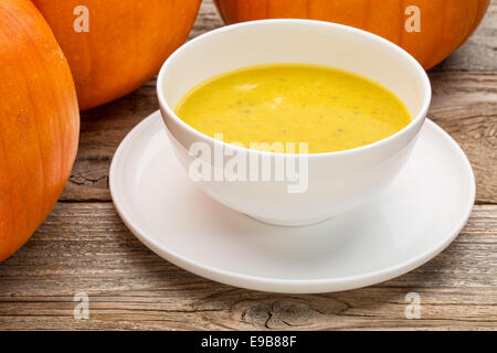 Kürbis Cremesuppe - eine Schale umgeben von Kürbissen auf einem rustikalen Holztisch Stockfoto