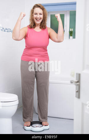 Glückliche Frau wiegen sich auf die Waage im Badezimmer Stockfoto