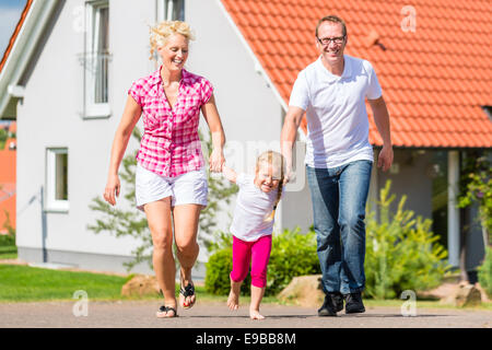 Familie von Eltern und Kind zu Fuß vor Haus im Dorf oder Stadtteil Stockfoto