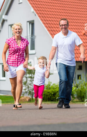 Familie von Eltern und Kind zu Fuß vor Haus im Dorf oder Stadtteil Stockfoto