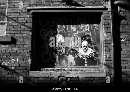 Ein Graffiti-Bild von einem unheimlich aussehende Clown auf die hölzerne Laderampe Tür einer heruntergekommenen Fabrik gemalt Stockfoto