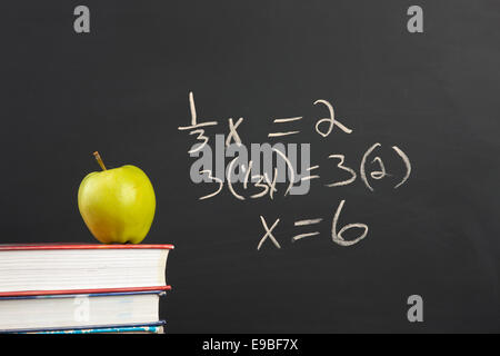 Ein Apfel auf Stapel von Büchern durch eine Algebra-Formel an der Tafel. Stockfoto