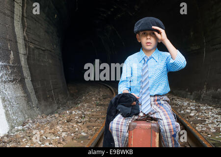 Kind in Vintage-Kleidung sitzt auf Eisenbahn Straße vor einem Tunnel. Stockfoto