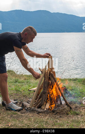 Junge, die zünden Feuer in einem Wald. See auf einem Hintergrund Stockfoto