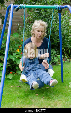 Großmutter mit zwei Jahre alten Enkelin, stieß sie auf Schaukel spielen. UK Stockfoto