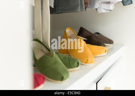 Reihe von neuen legere Kleidung auf Bügeln im Shop mit vier bunten Paar Schuhe unter ihm. Kleidung wie Garderobe vorgestellt. Stockfoto