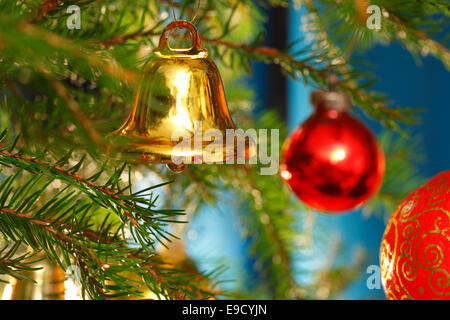 Eine goldene Glocke hängt zusammen mit roten Kugeln an den Weihnachtsbaum. Stockfoto