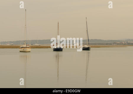 Drei Boote in einer Reihe mit Reflexionen im Meer, mit einem Leuchtturm im Hintergrund in Milford am Meer, England Stockfoto