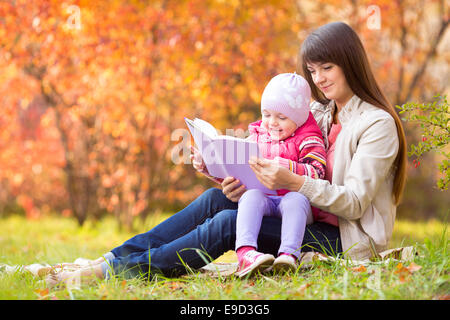 Mutter und Kind lesen ein Buch im Freien im Herbst Stockfoto