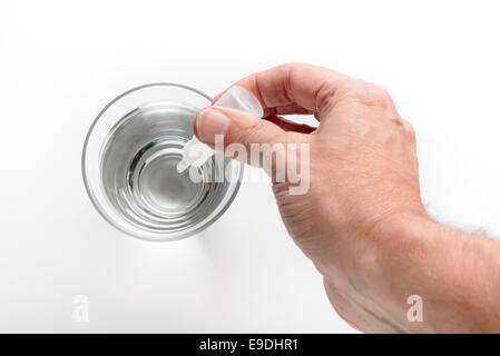 Die Hand des Menschen setzen Apotheke Tropfen in ein Glas transparent Wasser auf weißem Hintergrund Stockfoto