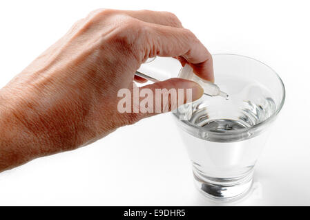 Die Hand des Menschen setzen Apotheke Tropfen in ein Glas transparent Wasser auf weißem Hintergrund Stockfoto