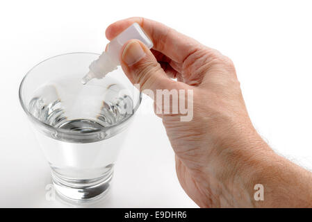 Die Hand des Menschen setzen Apotheke Tropfen in ein Glas transparent Wasser auf weißem Hintergrund Stockfoto