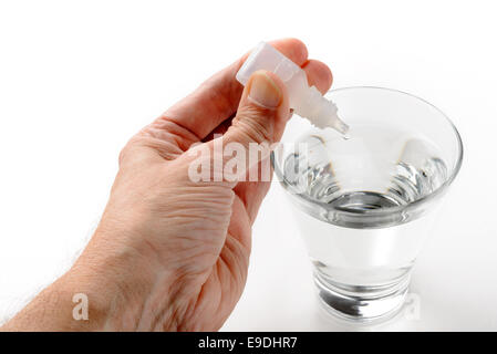 Die Hand des Menschen setzen Apotheke Tropfen in ein Glas transparent Wasser auf weißem Hintergrund Stockfoto