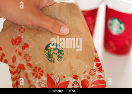 Frau Hand zum mitnehmen ein Starbucks Holiday Papiertüte mit zwei Urlaub Papier Tassen Espresso auf Hintergrund. Stockfoto