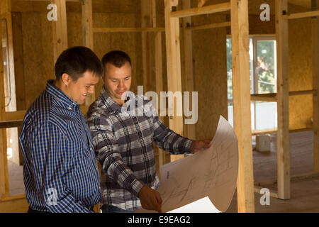 Zwei Bauherren innerhalb einer Hälfte abgeschlossen Holz Holzhaus steht, eine Diskussion über eine Blaupause des Gebäudes Stockfoto