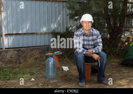 Müde, männliche Bauingenieur sitzt in der Ecke in Baustelle beim Baufortschritt betrachten. Stockfoto