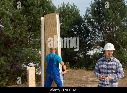 Bauarbeiter beschäftigt, Errichtung einer Ecke isolierte Holzwand Panel und Ingenieur vor Ort auf ein neues Haus zu bauen Stockfoto