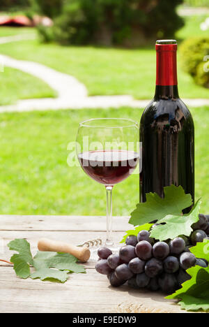 Rotweinglas und Flasche mit Weintraube im sonnigen Garten Stockfoto