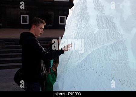 Kopenhagen, Dänemark. Okt. 2014. Nachdenklicher Junge, der die Magie des Inlandeises im öffentlichen Kunstwerk Ice Watch at the City Hall des dänisch-isländischen Künstlers Olafur Eliasson und Geologen Minik Rosing spürt. 100 Tonnen Binneneis wurden von Nuup Kangerlua Fiord, Nuuk, Grönland, in Kühlcontainern nach Kopenhagen transportiert. Das Schmelzen der zwölf großen Eisblöcke, die als Uhr geformt wurden, dient als Weckruf zur Klimaerwärmung: 100 Tonnen Inlandeis schmelzen jede 100stel Sekunde. Stockfoto