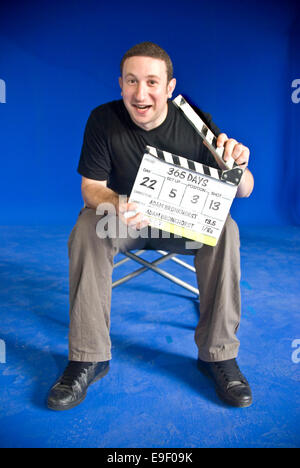 ein Mann sitzt auf einem Film-set mit einem blauen Bildschirm und eine Klappe Stockfoto