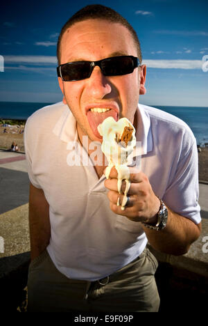 ein Mann isst und Eis und es schmilzt seine Hände an einem heißen Tag am Strand Stockfoto
