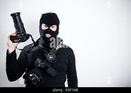 ein Fotograf, gekleidet in eine Sturmhaube, sah aus wie eine militärische Terrorist, mit Kamera, Belichtungsmesser, Objektivdeckel, Stockfoto