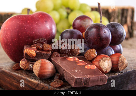 Jede Menge Obst Äpfel und Trauben mit Nüssen, Schokolade, Schokolade mit Nüssen Rosinen Apfel und Trauben auf hölzernen Hintergrund Stockfoto