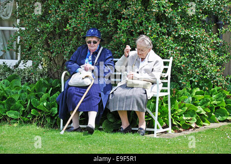 Zwei alte Damen mit Stöcken, sitzen auf einer Bank im Garten draußen ein Landhaus in Surrey, England, UK. Stockfoto