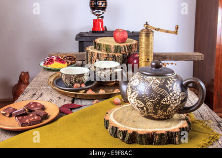 Tassen Tee auf alten Holztisch mit Äpfeln, Nüssen, Würfel von Schokolade und Tee Topf neben ihnen im Herbst Dekoration Stockfoto