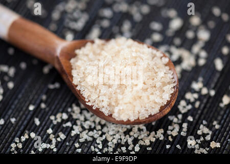 Brauner Rohrzucker Kristalle in einem Holzlöffel auf schwarzen Serviette. Stockfoto