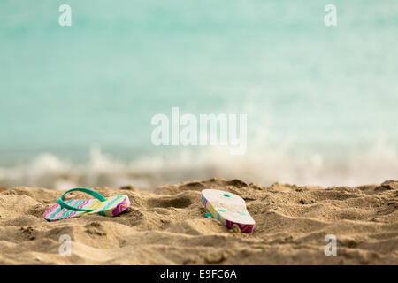 Ausrangierte Flipflops am Sandstrand vom Ozean Stockfoto