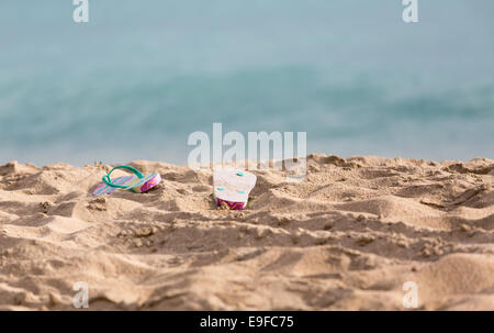 Ausrangierte Flipflops am Sandstrand vom Ozean Stockfoto