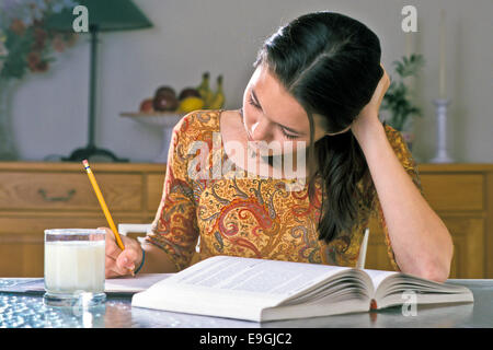 Hawaiian-Caucasian Mädchen in Gelb, Grün, Rot paisley Dress ihr Kopf auf ihre Hand schreiben Bericht Mädchen am Tisch. Herr © Myrleen Pearson Stockfoto