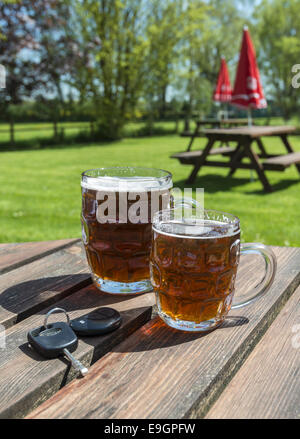 Autoschlüssel und Pints Bier auf einem Gartentisch aus Holz Bier Stockfoto