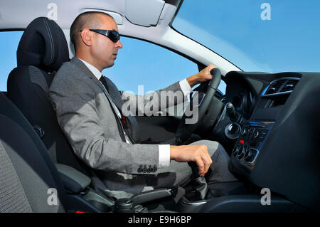 ein junger Mann trug einen Anzug und Sonnenbrille Autofahren mit Schaltgetriebe Stockfoto