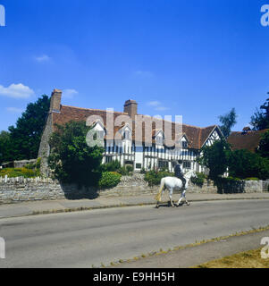 Eine Reiterin, die an Mary Ardens Cottage, Mary Ardens Farm, Wilmcote, Stratford-upon-Avon, Warwickshire, England vorbeikommt. Stockfoto