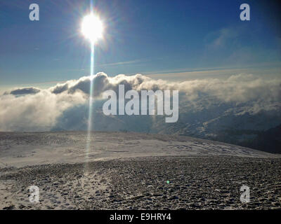 Sonne durch die Wolken vor dem Hintergrund eines blauen Himmels über einen schneebedeckten Berg Stockfoto
