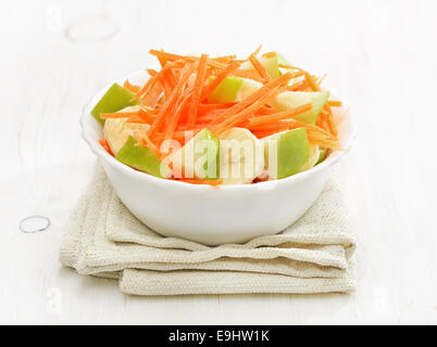 Gemüse Obstsalat mit Karotten, Äpfel, Bananen in Schüssel auf weißer Holztisch Stockfoto