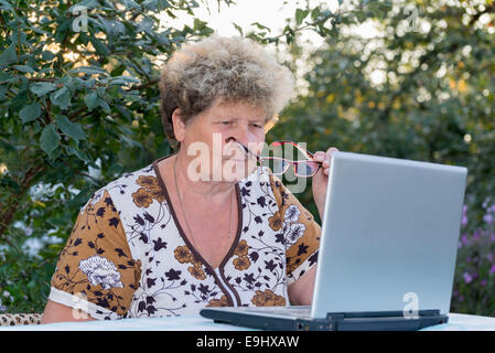 ältere Frau, die auf Computer im Garten arbeiten Stockfoto