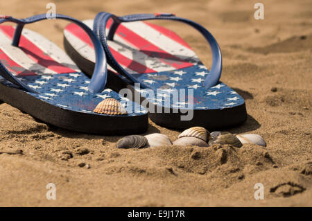 Flip Flops am Strand mit Muscheln und Meer im Hintergrund Stockfoto