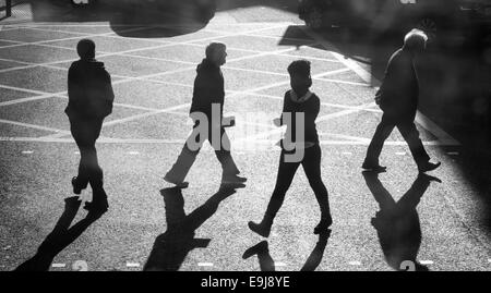 Vier Menschen überqueren einer viel befahrenen Straße in London an einem sehr sonnigen Tag. Stockfoto