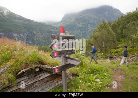 Zwei junge männliche Wanderer auf Homlong Hof hoch oben über dem Geiranger Fjord, Norwegen. Stockfoto