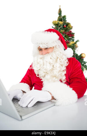 Santa mit seinem Laptop in der Nähe von Weihnachtsbaum Stockfoto