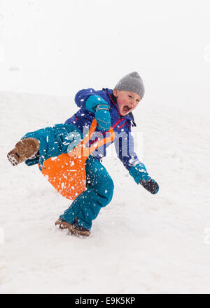 kleinen lachenden jungen schnell hinunter einen steilen Hügel in einer Wolke aus Schnee Rodeln Stockfoto